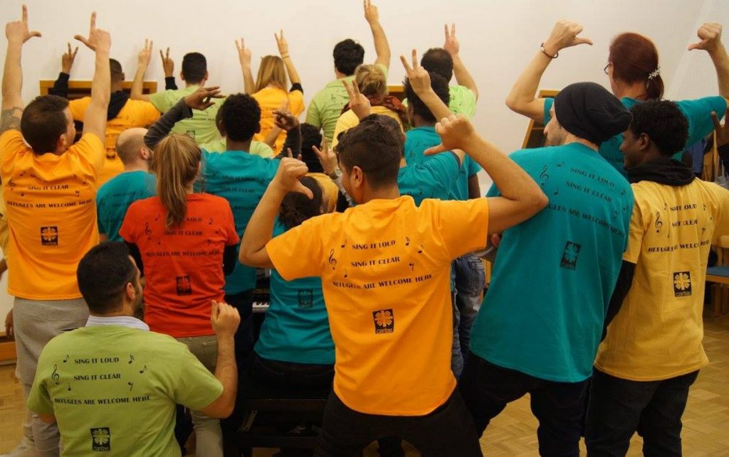 Foto von Chormitgliedern in bunten T-Shirts mit Aufdruck "Sing it loud, sing it clear, refugees are welcome here